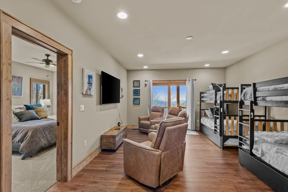 This image showcases a cozy den area featuring bunk beds, reclining chairs, a television, and large windows letting in natural light. The arrangement clearly supports group relaxation and family gatherings, with visible sleeping accommodations and entertainment amenities.