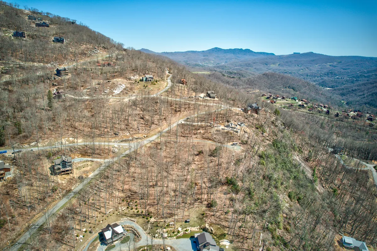 This image features a sweeping mountainous landscape dotted with scattered houses and intersected by curved roads. The open terrain and distant peaks evoke a sense of adventure and exploration, with visual hints of hiking opportunities and high-country vistas. The setting is tranquil and expansive, inviting viewers to imagine outdoor activities amidst the natural beauty.