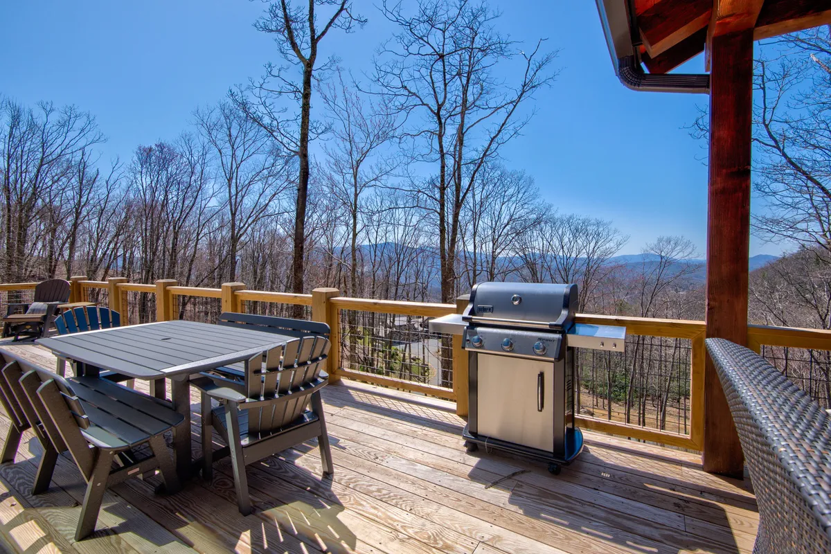 This image presents an outdoor dining set on a wooden deck with a grill and mountain views in the background. The ambiance is ideal for al fresco meals, whether it's morning coffee or sunset dinners with friends and family.