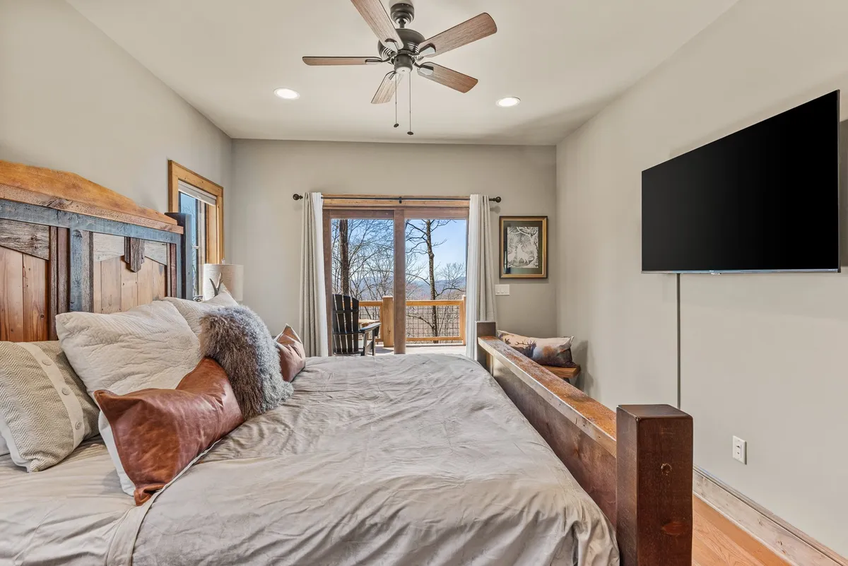 A tranquil bedroom with a king-sized bed adorned with decorative pillows, a large window offering a picturesque view, and a wall-mounted television for in-room entertainment. The space feels airy, inviting, and designed for restful relaxation.