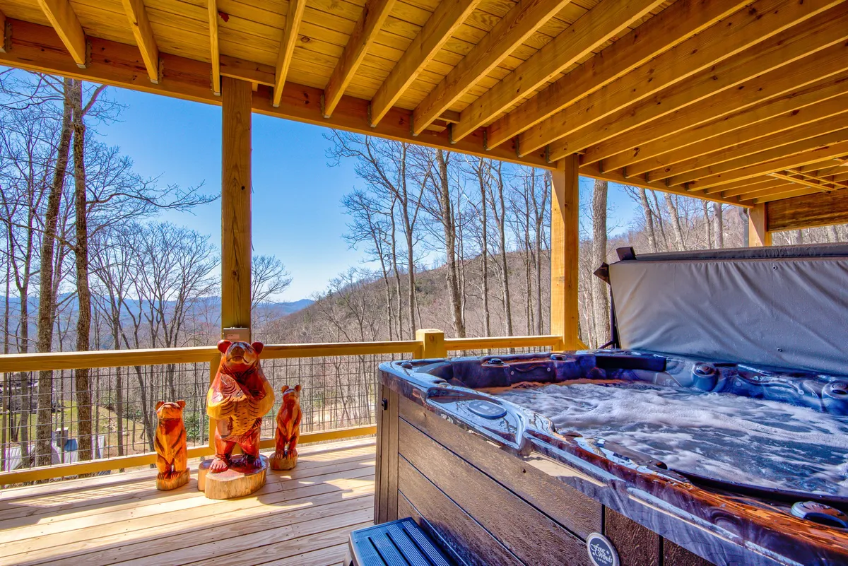 A tranquil scene with a hot tub set on a wooden deck, flanked by whimsical wooden bear sculptures, and overlooking a panoramic mountain view. The atmosphere is peaceful and inviting, perfect for unwinding after a day of adventure.