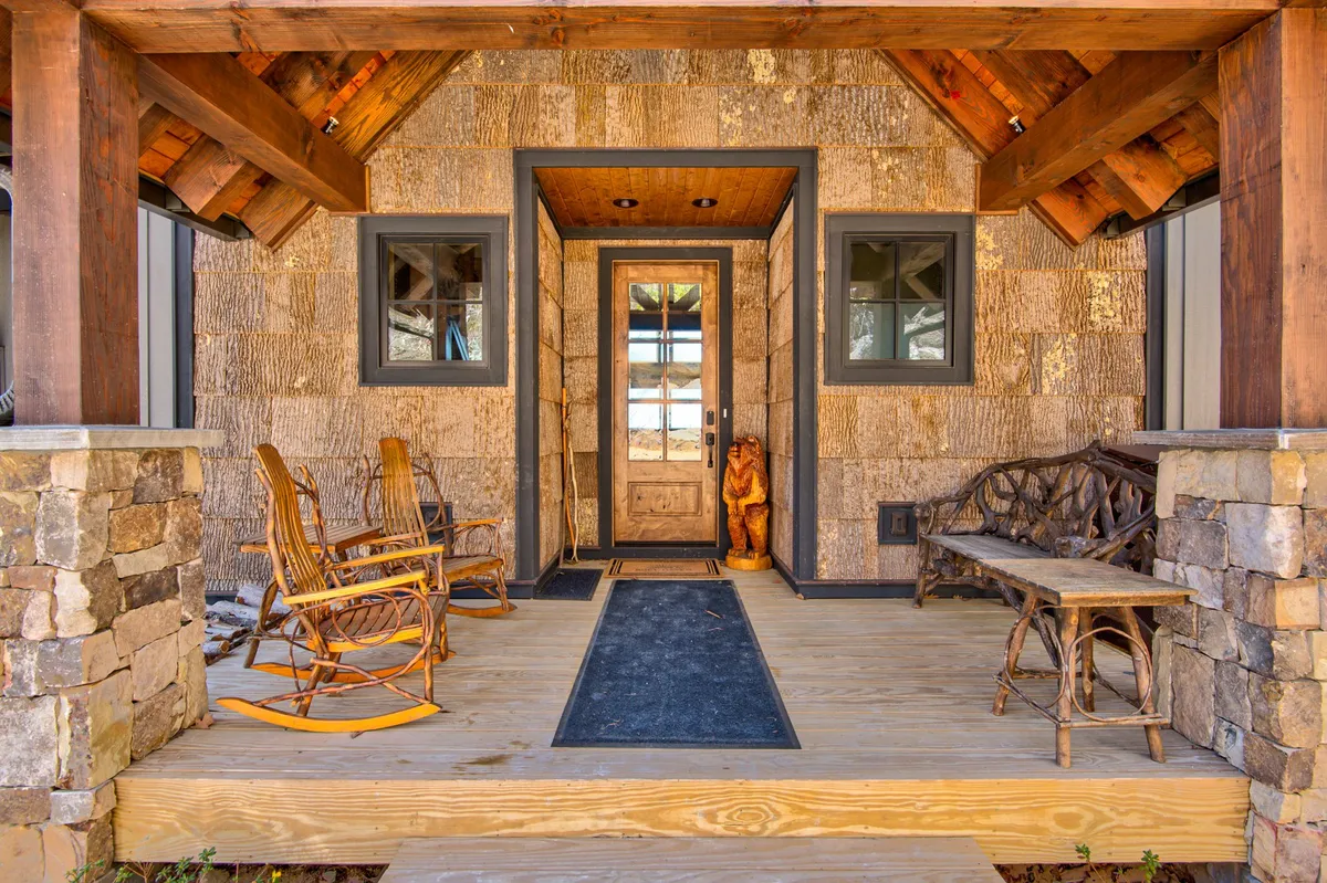 The image shows the welcoming front entrance of Rock Haven, featuring classic rocking chairs, a wooden bench, and a charming bear statue. The porch exudes a friendly, inviting atmosphere perfect for relaxing and greeting guests, hinting at a space where both people and pets can feel at home before heading out for adventure.